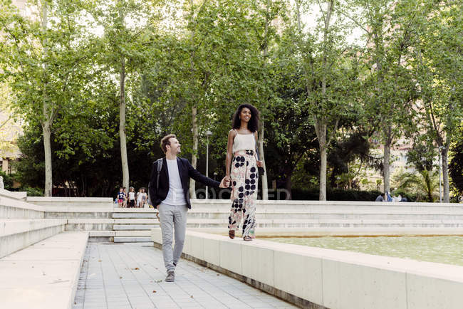 Charming black woman smiling and walking on fountain border with boyfriend in park — Stock Photo