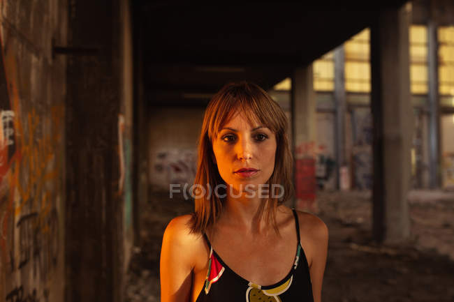Serious young woman standing in sunset light in abandoned building — Stock Photo