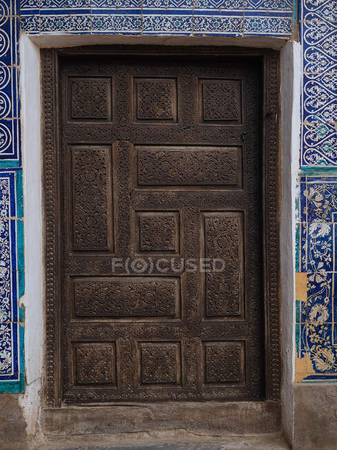 Внешний снимок высеченной деревянной двери с удивительным декором голубой плитки вокруг, Узбекистан — стоковое фото