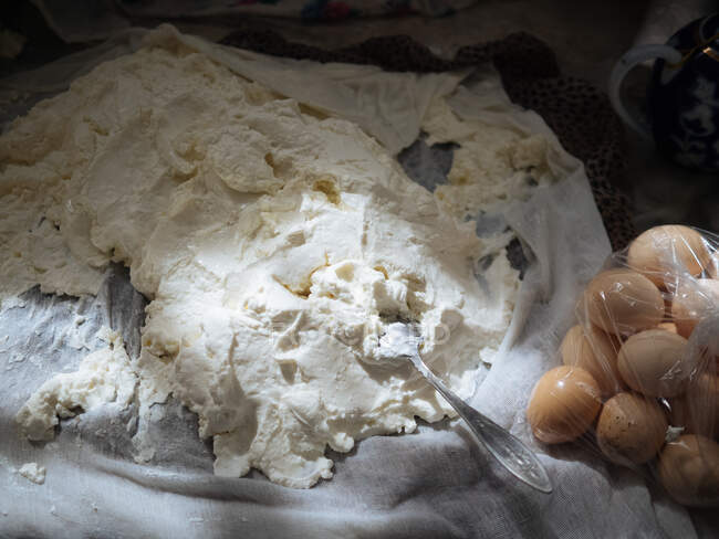 De arriba tiro de queso blanco hecho a mano para untar arreglado sobre textil blanco con huevos en bolsa, Uzbekistán - foto de stock