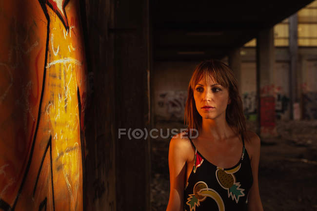 Серьезная молодая женщина, стоящая на закате в заброшенном здании — стоковое фото