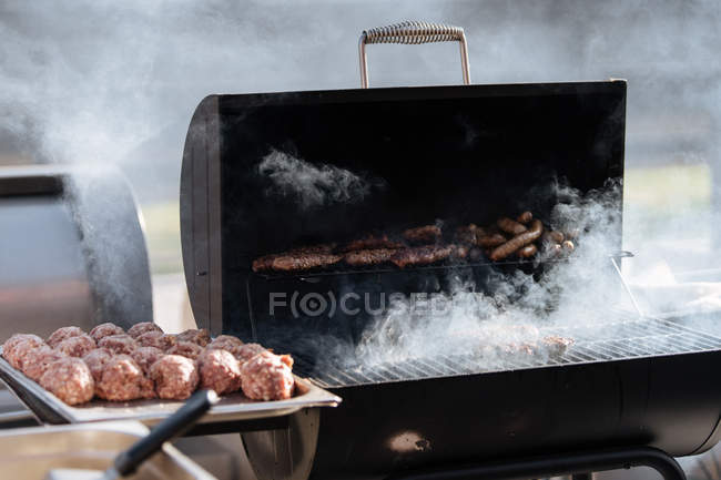 Hambúrgueres crus assar na grade de churrasqueira ao ar livre — Fotografia de Stock
