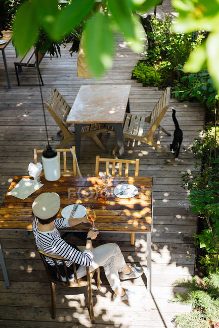 Mujer elegante en ropa de verano elegante copa de vino en la mesa de madera en la cafetería al aire libre - foto de stock