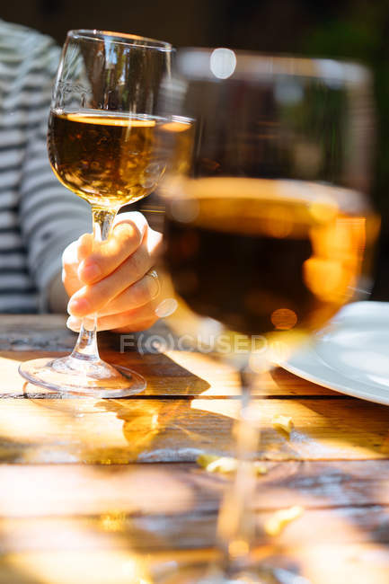 Human hand holding glass of white wine on wooden table outdoors — Stock Photo