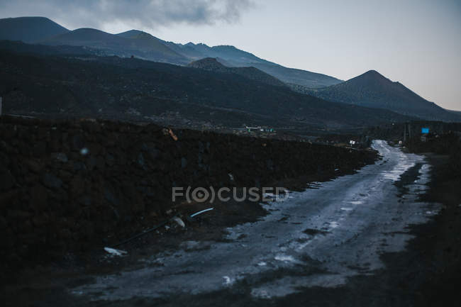 Landscape of wet remote road in rocky dark terrain with silhouette of mountains, La Palma, Spain — Stock Photo