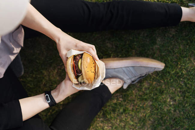 Женщина держит бургер, сидя на траве — стоковое фото