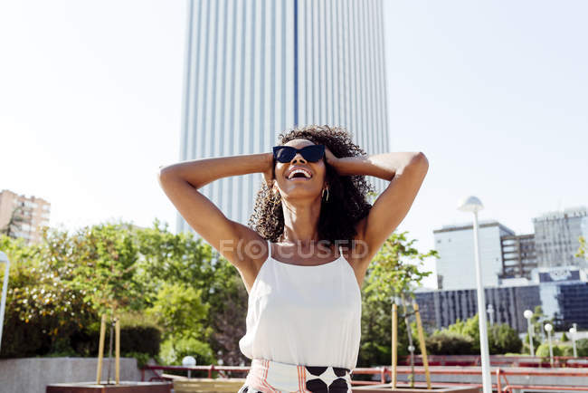 Elegant African-American woman laughing while walking on street of modern city on sunny day — Stock Photo