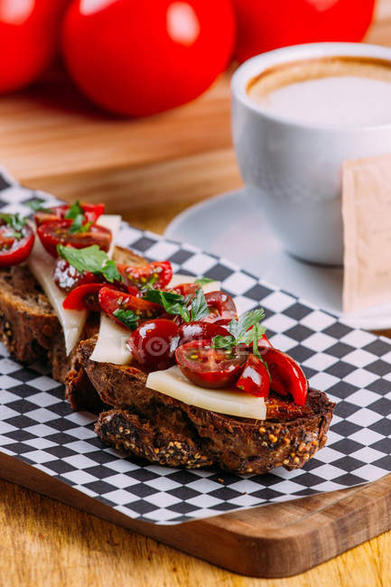 Brown bread sandwich with cheese and tomatoes on checkered napkin — Stock Photo