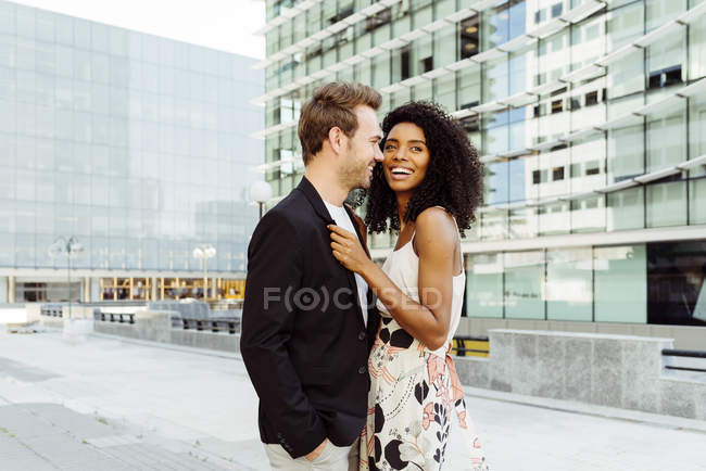 Sonriente pareja multirracial de pie en la ciudad moderna juntos - foto de stock