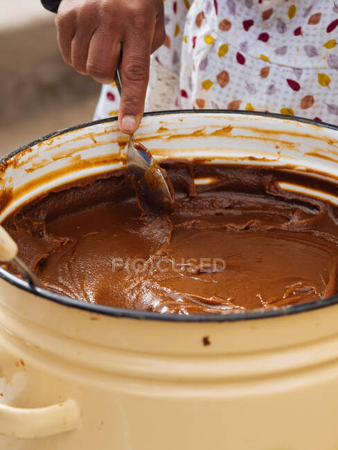 Recorte en primer plano de la persona revolviendo con cuchara masa dulce de leche caramelizada en olla de metal, Uzbekistán - foto de stock