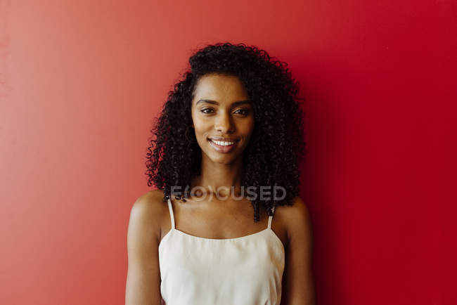 Портрет улыбающейся афроамериканки, стоящей на красном фоне — стоковое фото