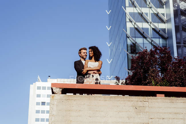 Многорасовая пара обнимается перед современными зданиями — стоковое фото