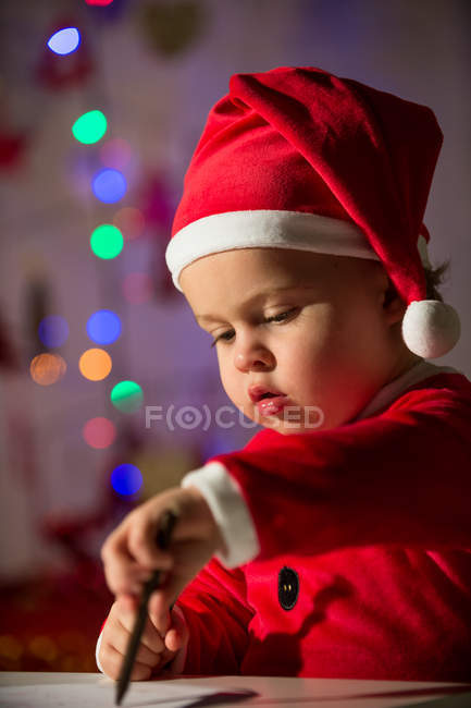 Happy little child in Christmas clothes drawing with pencil — Stock Photo
