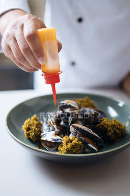 Шеф-кухар капає з соусом північних морепродукти блюдо з мідіями на тарілку — стокове фото