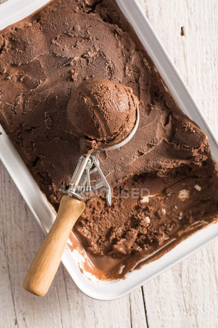 Домашнее шоколадное мороженое в коробке с совок на деревянной поверхности — стоковое фото