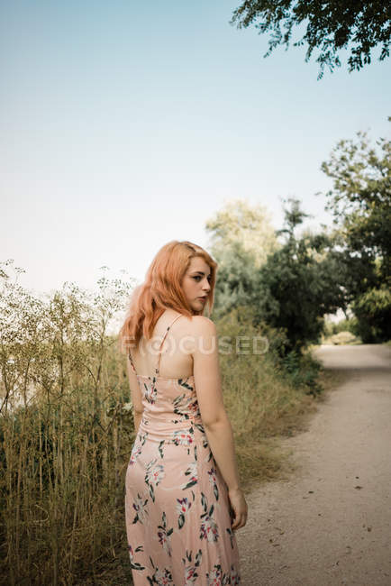 Jovem mulher de vestido olhando sobre o ombro na estrada rural — Fotografia de Stock