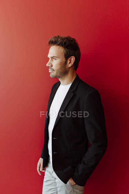 Nachdenklicher Mann im eleganten Outfit steht auf leuchtend rotem Hintergrund — Stockfoto