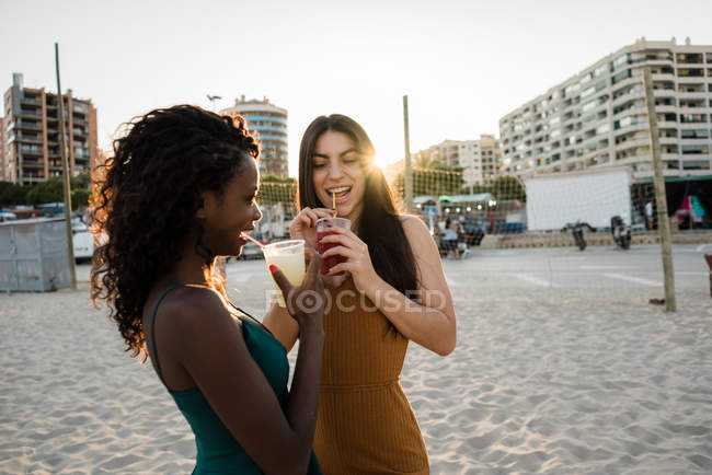 Jeunes femmes dégustant des boissons sur la plage de la ville au soleil — Photo de stock