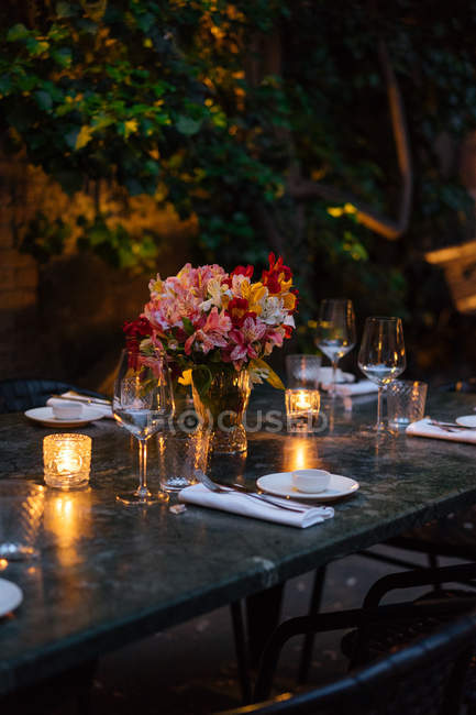 Mesa decorada con velas y flores por la noche en el patio trasero - foto de stock