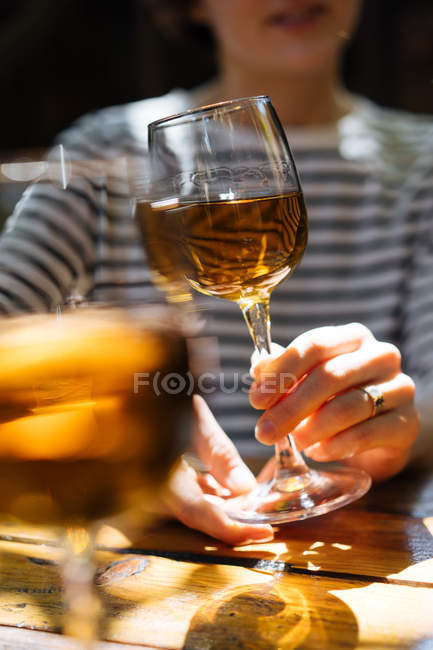 Mains féminines tenant un élégant verre de vin blanc sur une table en bois à l'extérieur — Photo de stock