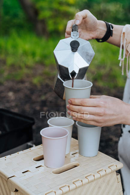 Manos femeninas vertiendo café recién hecho de la cafetera en tazas en el picnic - foto de stock