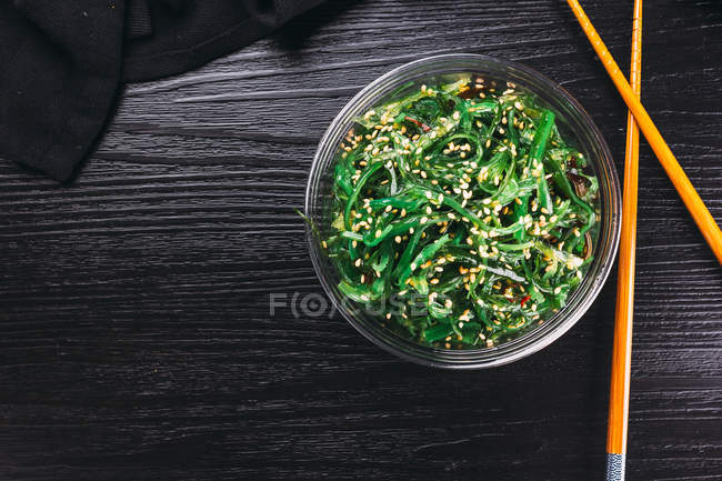 Палички та миска смачного салату з морських водоростей на чорній дерев'яній стільниці — стокове фото