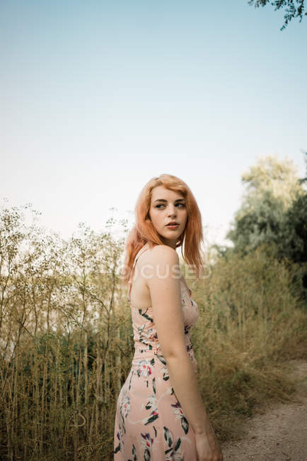 Mujer joven en vestido mirando por encima del hombro en el camino del campo - foto de stock