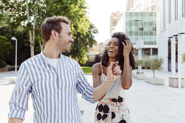 Couple riant tenant la main tout en marchant dans le parc de la ville — Photo de stock