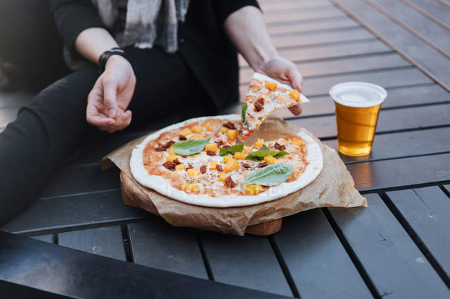 Жінка сидить на вулиці зі склянкою пива і запечена смачна піца — стокове фото