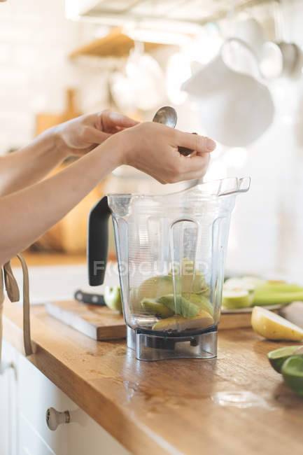Mains féminines mettant des fruits dans un bol mélangeur pour smoothie vert — Photo de stock