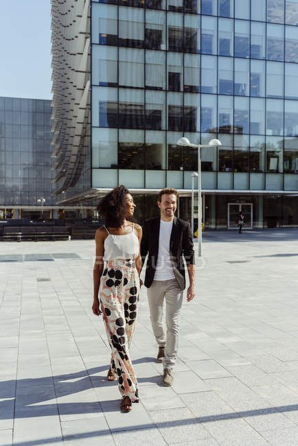 Elegantes multiethnisches Paar hält Händchen, während es in der modernen Stadt spaziert — Stockfoto
