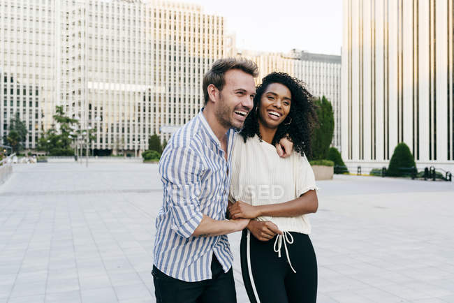 Allegro coppia multirazziale abbracciare e ridere mentre si cammina sulla strada della città insieme — Foto stock