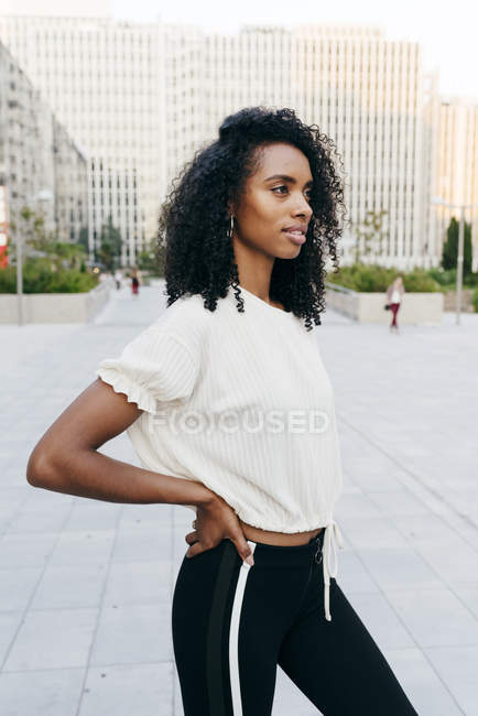 Pensativa mulher afro-americana de pé na rua com as mãos no quadril — Fotografia de Stock