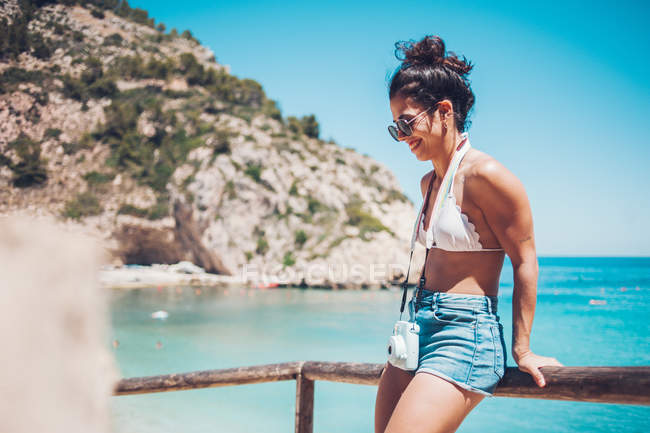 Lächelndes junges Mädchen in Sommerkleidung lehnt am Holzgeländer am Strand — Stockfoto