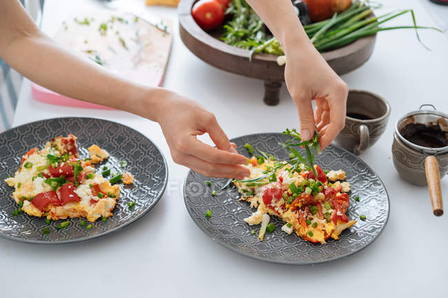 Human hands sprinkling with onion omelette with vegetables on plate — Stock Photo