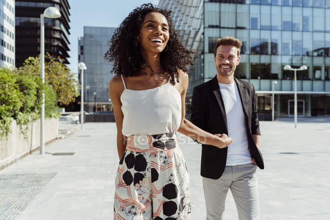 Happy multiracial couple smiling and holding hands while walking on modern city street together — Stock Photo