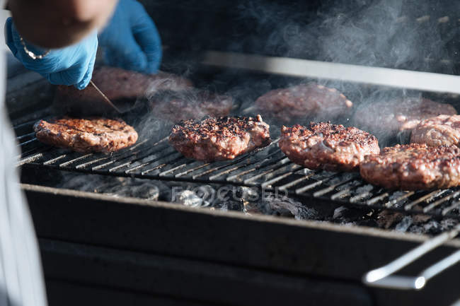 Human hands cooking raw burger patties roasting on grid of barbecue grill outdoors — Stock Photo