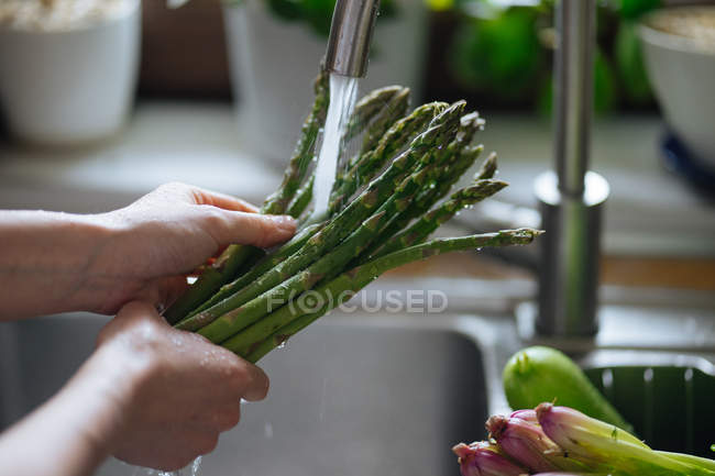 Female hands washing fresh green asparagus in kitchen sink — Stock Photo