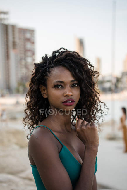 Junge afrikanisch-amerikanische Frau mit Locken blickt in die Kamera an der Küste — Stockfoto