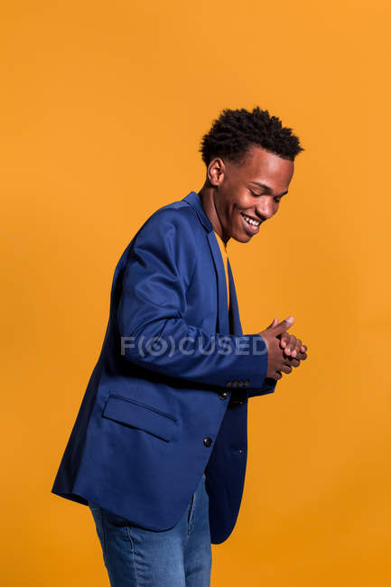 Черный мужчина в куртке и джинсах смеется на оранжевом фоне — стоковое фото