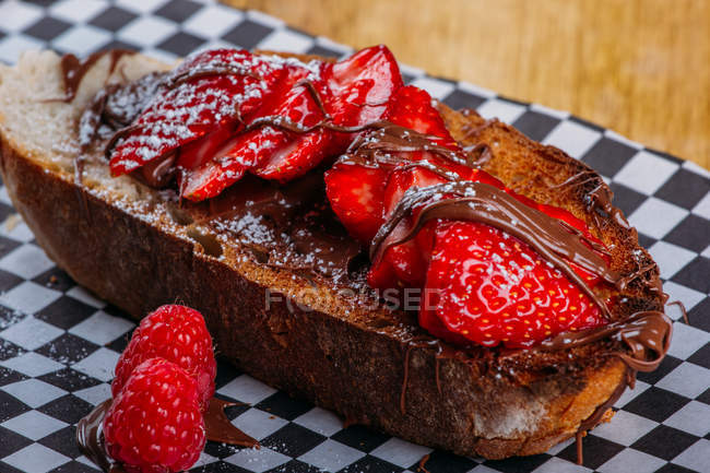 Gros plan de pain grillé croustillant aux fraises mûres et sauce au chocolat servie sur papier — Photo de stock
