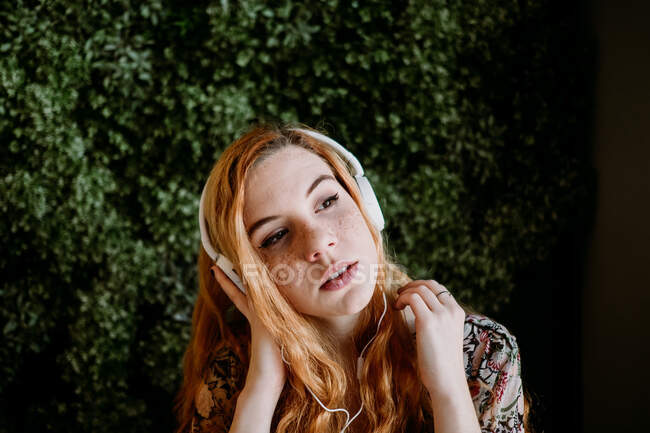 Pretty young redhead woman putting on headphones at the bush. — Stock Photo