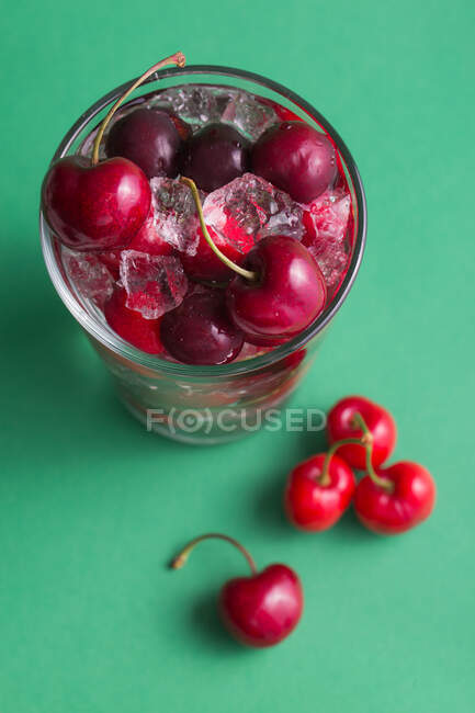 Cherries in a glass with ice on green background — Stock Photo