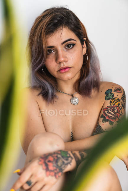 Jeune femme nue avec le corps couvert de tatouages regardant la caméra — Photo de stock