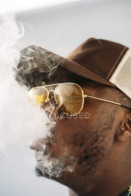 Homem elegante preto usando óculos de sol. Ele está vaping com um cigarrete eletrônico ao ar livre — Fotografia de Stock