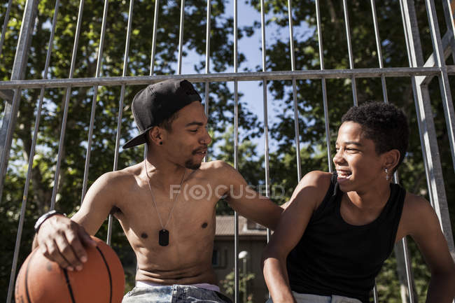 Afro jóvenes hermanos sentados con baloncesto en la cancha al aire libre y abrazando - foto de stock