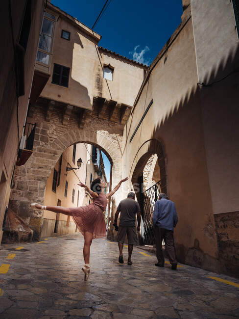 Vista lateral de dançarina de balé muito feminina de pé e posando na rua ensolarada. — Fotografia de Stock