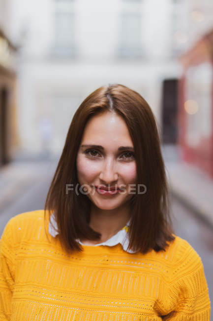 Улыбающаяся женщина в желтом кардигане стоит на улице и смотрит в камеру — стоковое фото