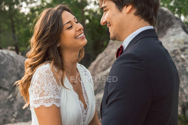 Crop side view of cheerful tender man and woman touching with noses and looking at each other with love in wedding day — Stock Photo