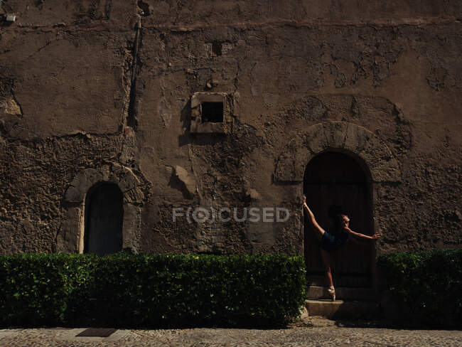 Вид збоку красива балерина, що стоїть і позує біля старовинних дверей . — стокове фото